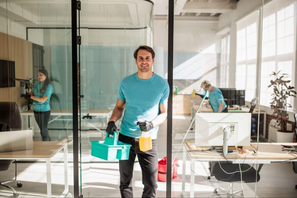 Commercial cleaning company crew wiping down desks and glass partitions in an open office.