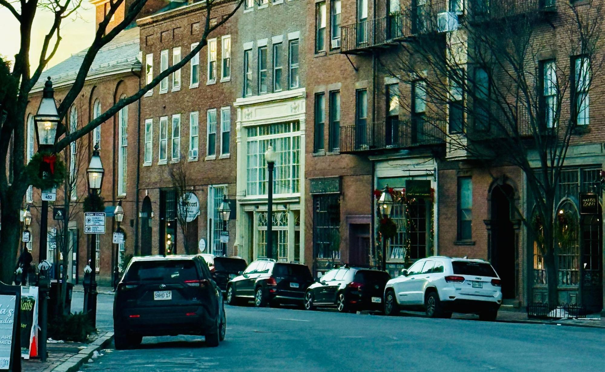 Brick storefronts and parked cars along a historic New England main street at dusk